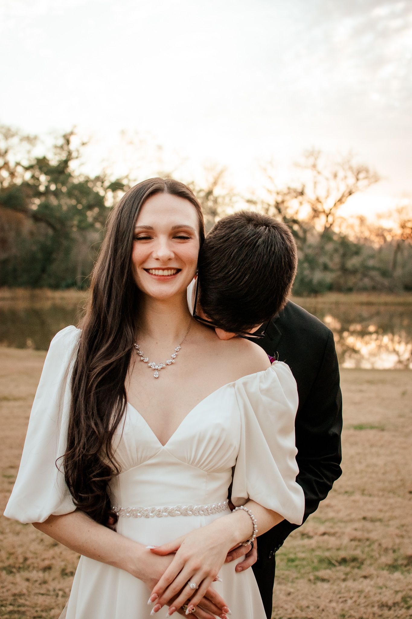 Bride in elegant white dress with bishop sleeves smiles radiantly during golden hour portrait session.