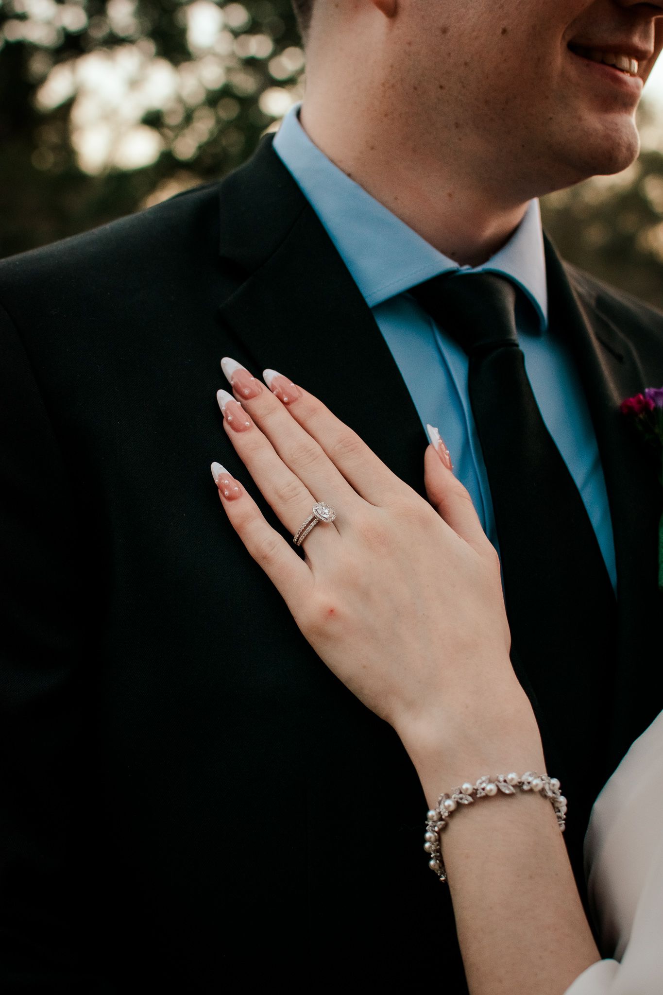 Detail shot of bride's hand with wedding ring resting on groom's lapel.