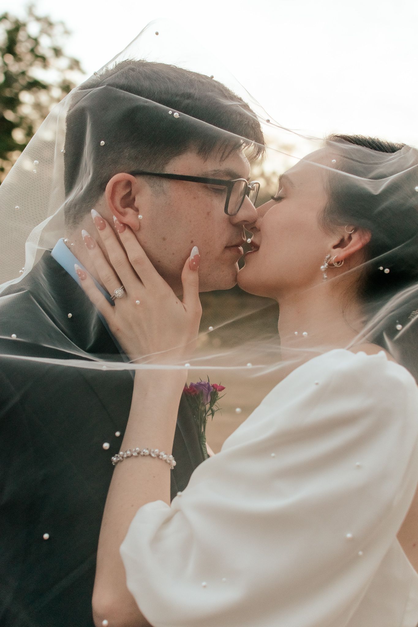 Romantic kiss captured through delicate wedding veil during golden hour.