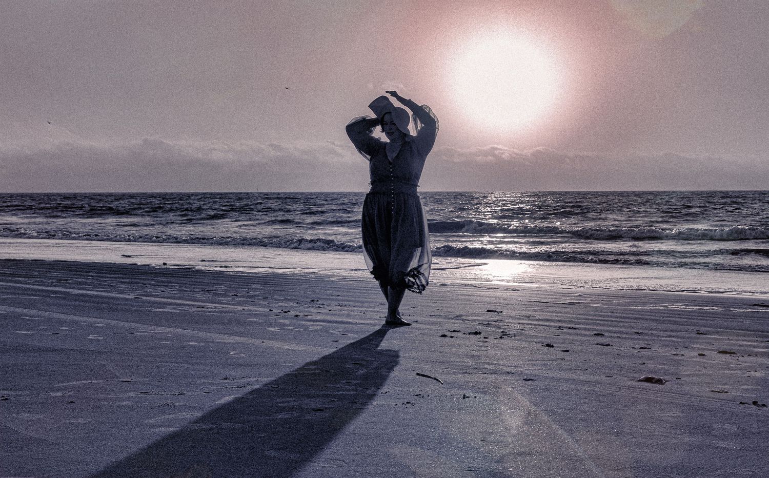 Silhouetted figure walking on beach at sunset creating long shadow on sand.