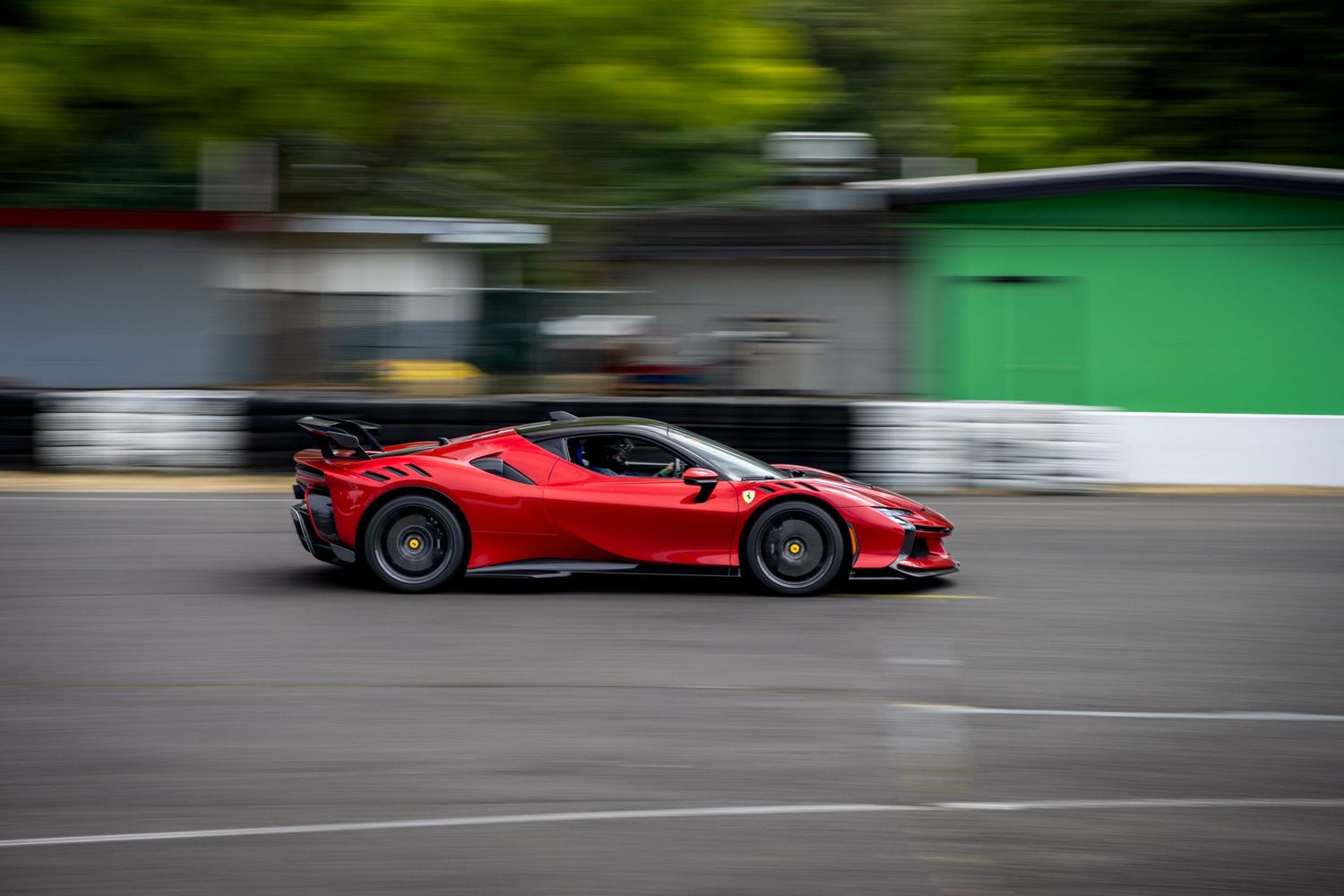 Red Ferrari sports car in motion blur on a street with green buildings in the background.