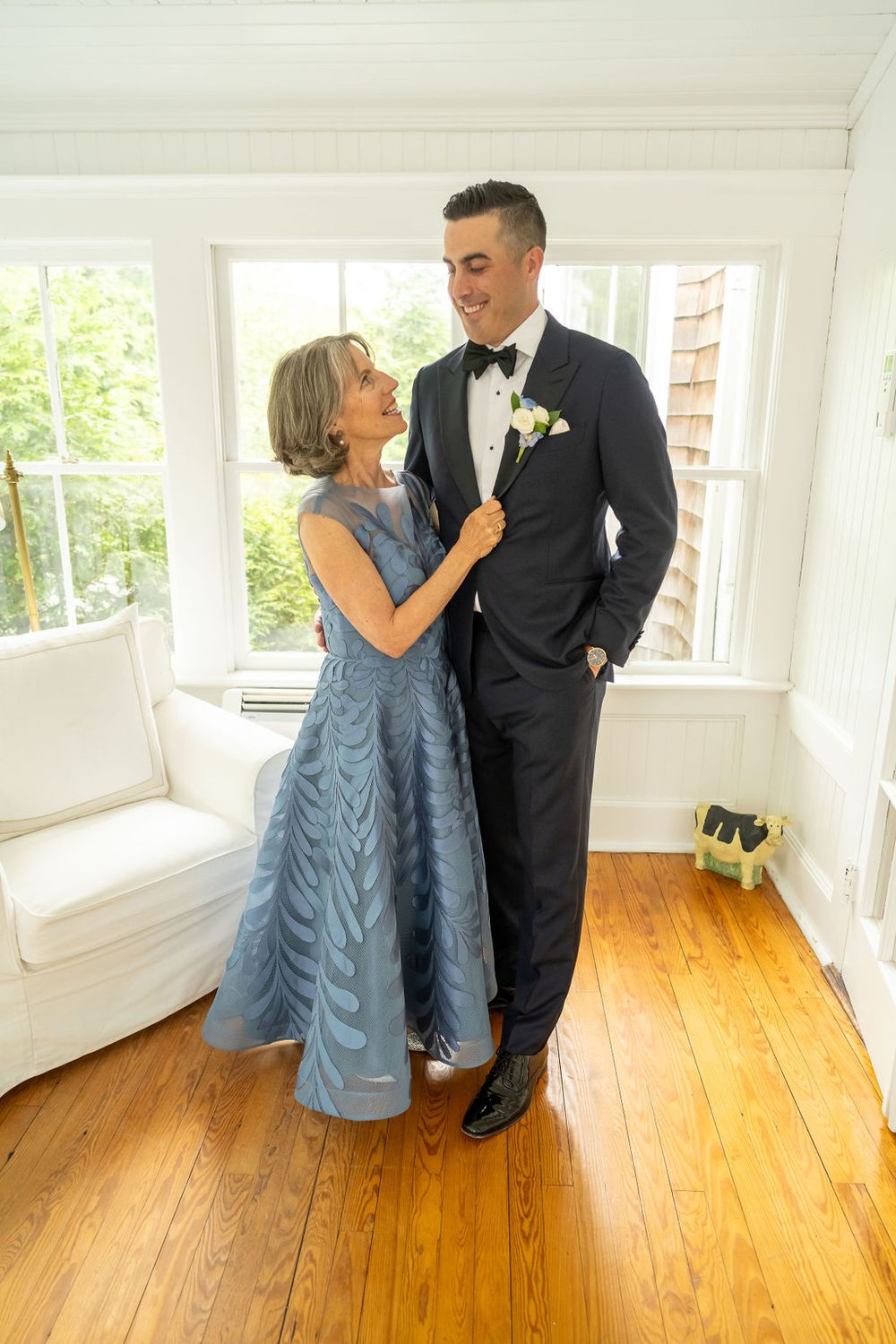 Elegant mother-son dance moment with groom in black tuxedo and mother in blue gown at bright indoor venue.