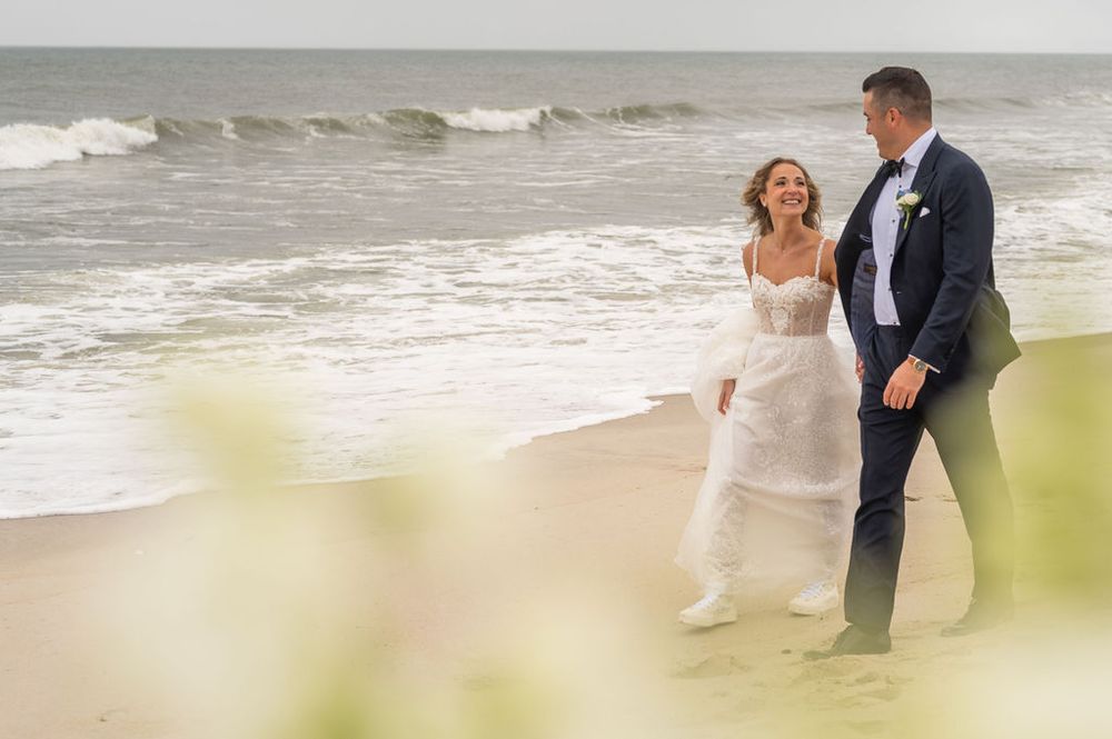 Newlyweds stroll along the shoreline smiling at each other on their wedding day.