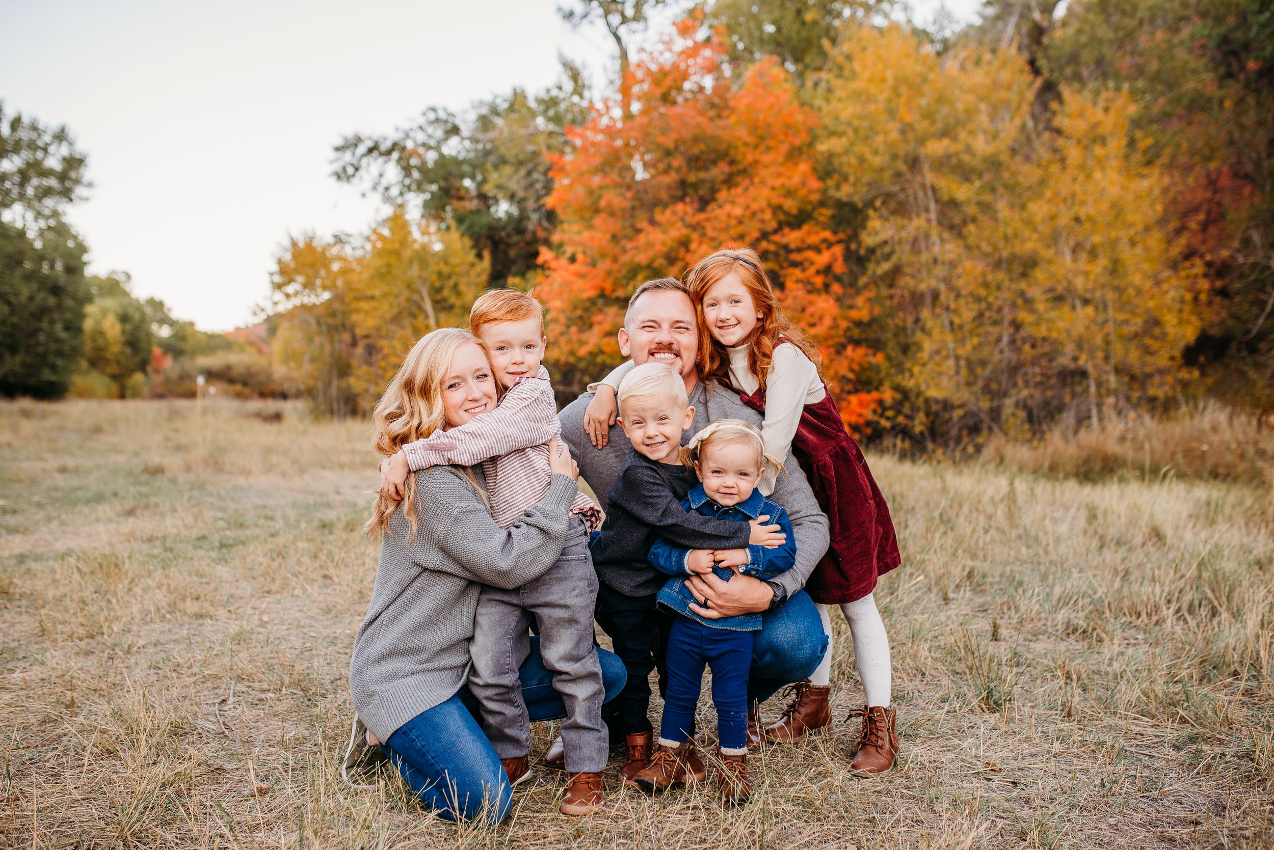 Family group hugging and laughing together against autumn foliage background.