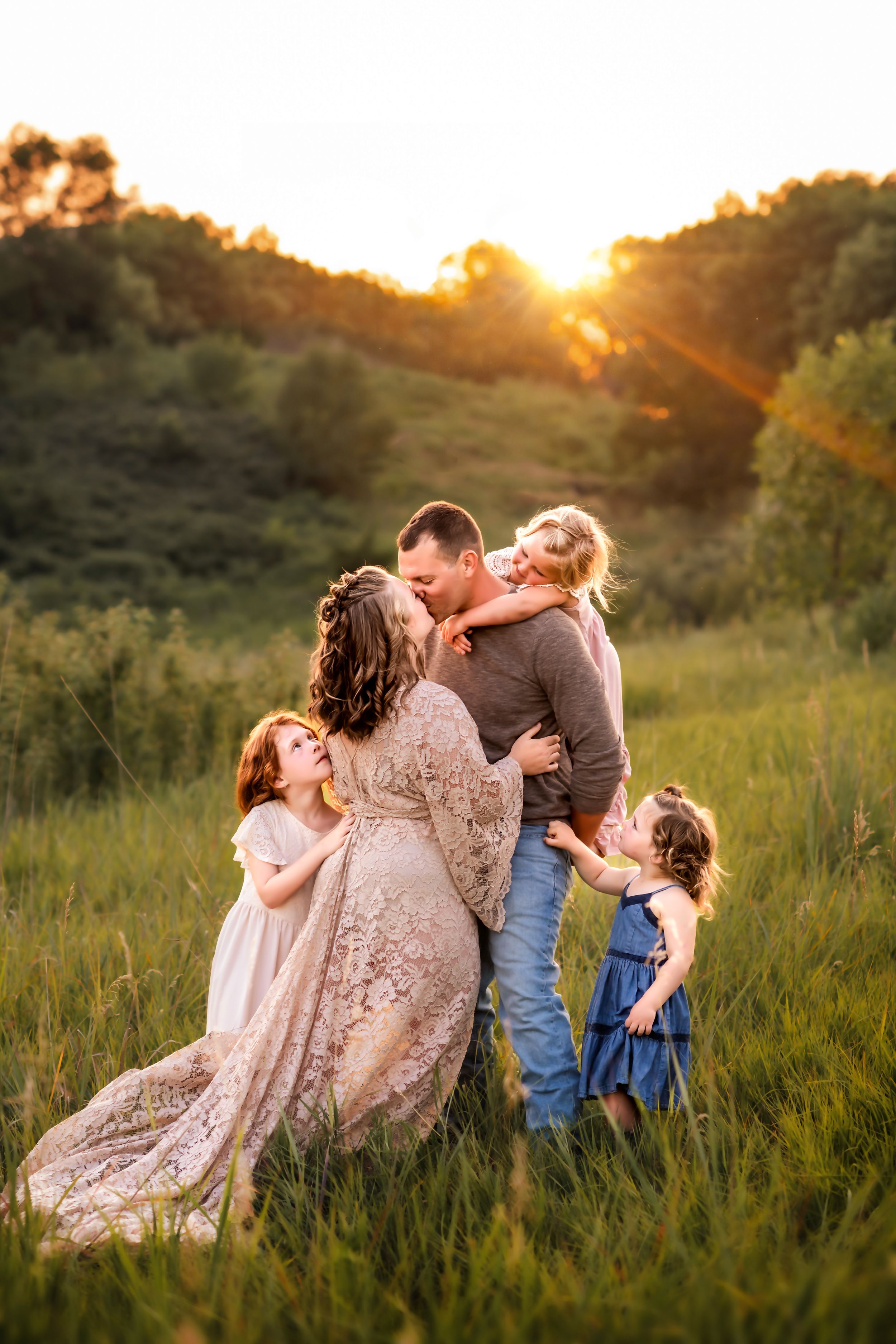 Family shares intimate moment together in tall grass during golden hour sunset.