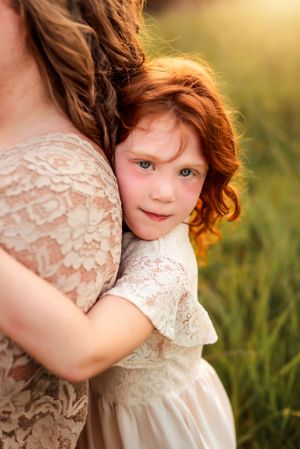 Young child in lace dress cuddles close to someone in matching attire during golden hour.