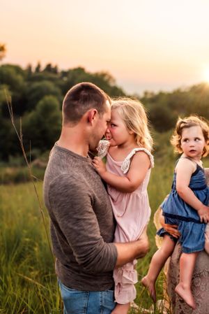Family shares tender moments together in a grassy field at sunset.