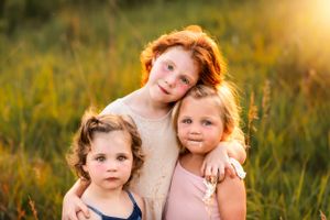 Three children pose together in golden sunlit field during sunset photo session.