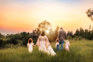 Family walking hand in hand through meadow at sunset silhouetted against golden sky.