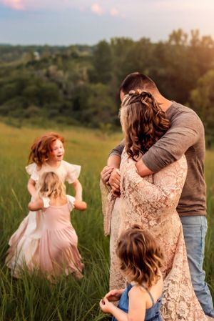 Family sharing playful moment together in tall grass during sunset photoshoot.