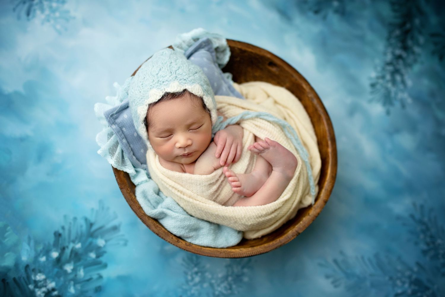 Peaceful sleeping newborn wrapped in soft blue blanket on wooden bowl backdrop.