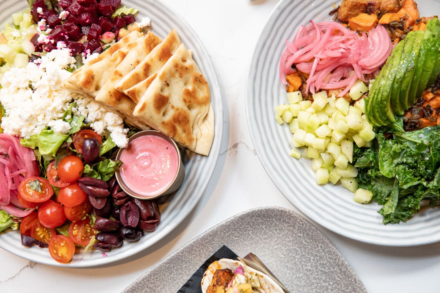 Colorful grain bowls with pickled vegetables, tomatoes, and leafy greens on striped plates.