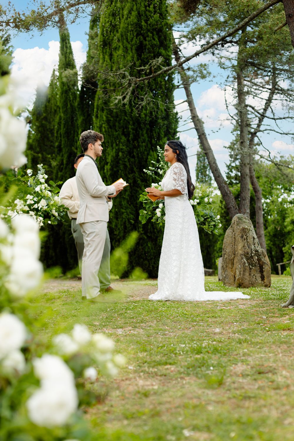 Intimate wedding ceremony moment in a garden setting with tall cypress trees and natural greenery.