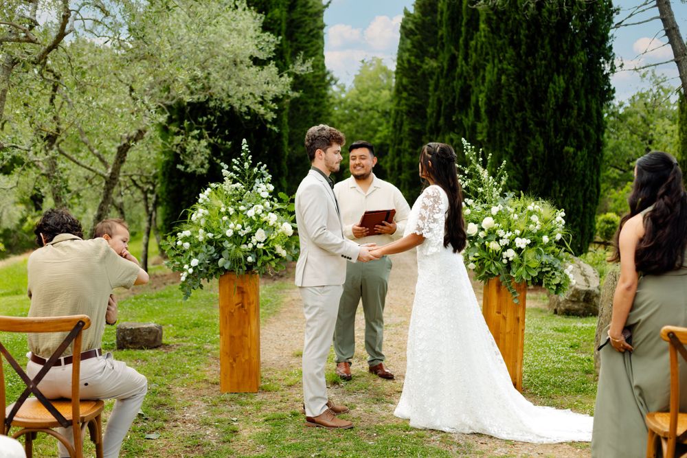 Wedding couple sharing a first look moment in a garden setting with cypress trees and white floral decorations.