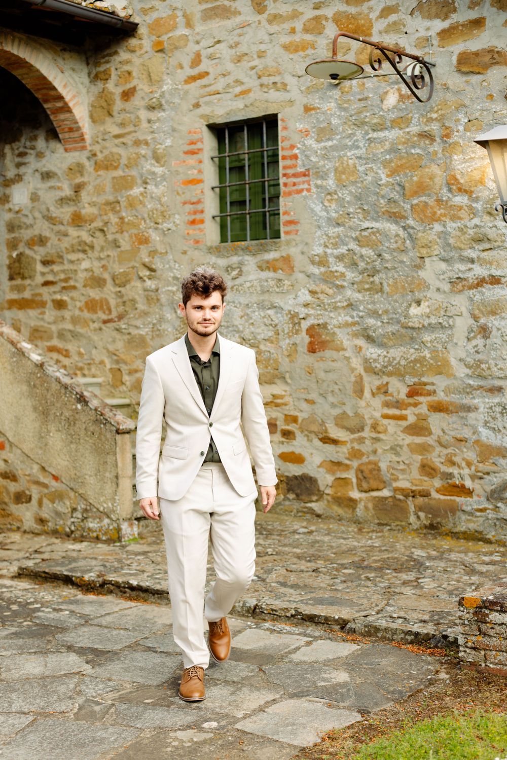 Person in white suit walking along stone wall of rustic building.