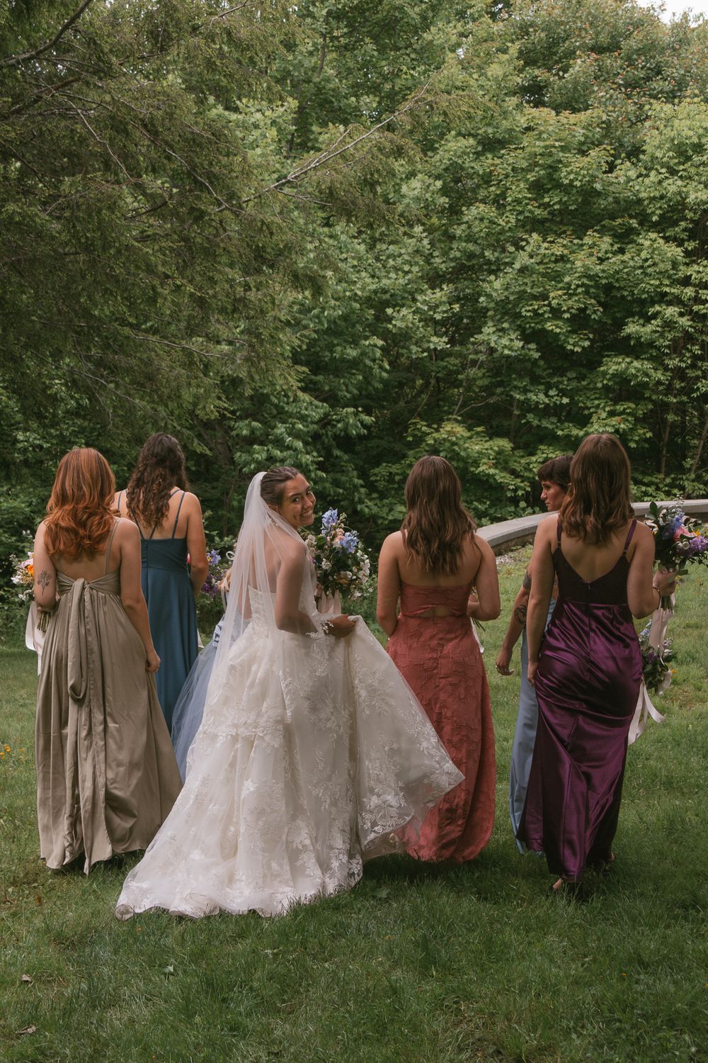 Back view of bridesmaids in varied dresses walking together on grass. Boone NC wedding photographer