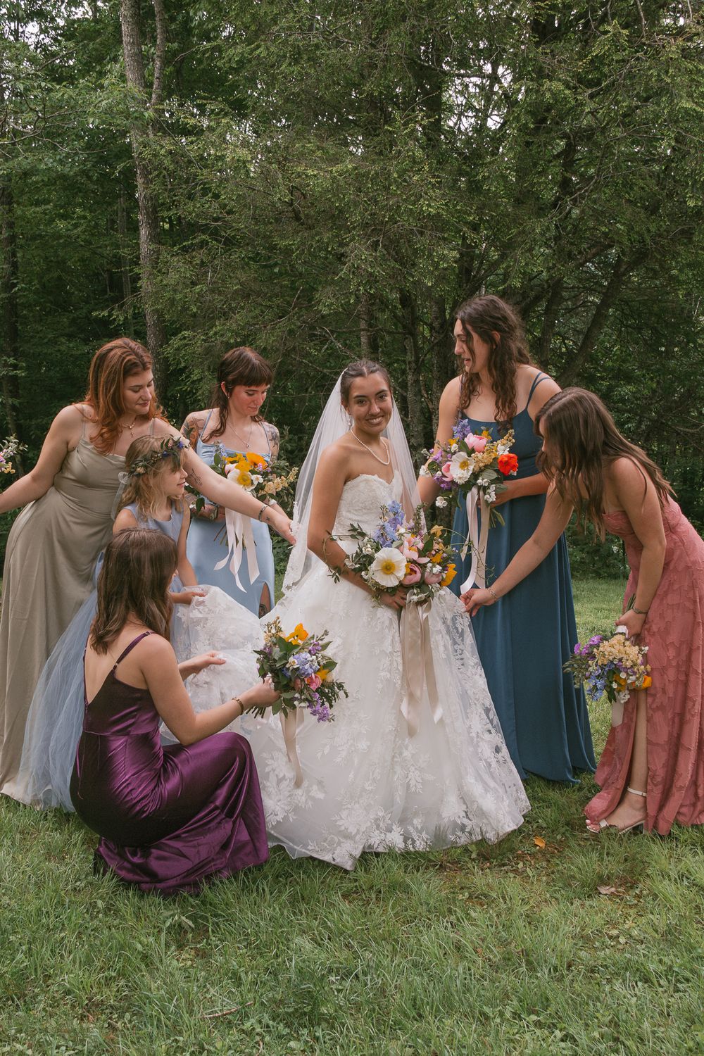 Wedding party in colorful dresses sitting together on grass for casual photos. Boone NC wedding photographer