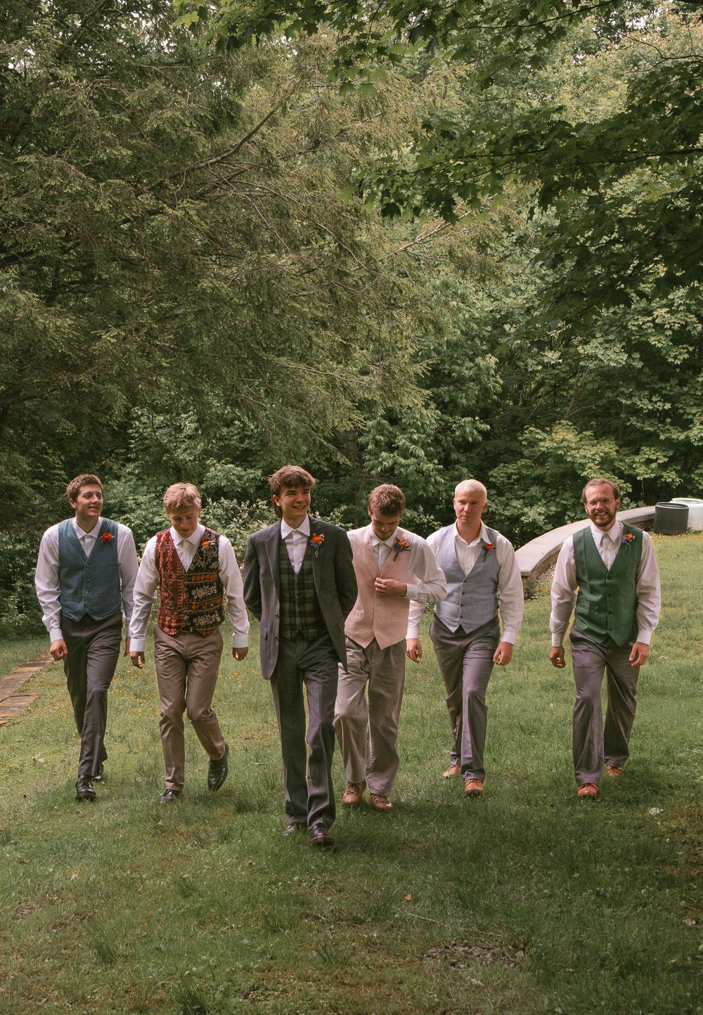 Group poses playfully in a line on grassy field wearing vintage-style attire. Historic venue wedding photographer North Carolina