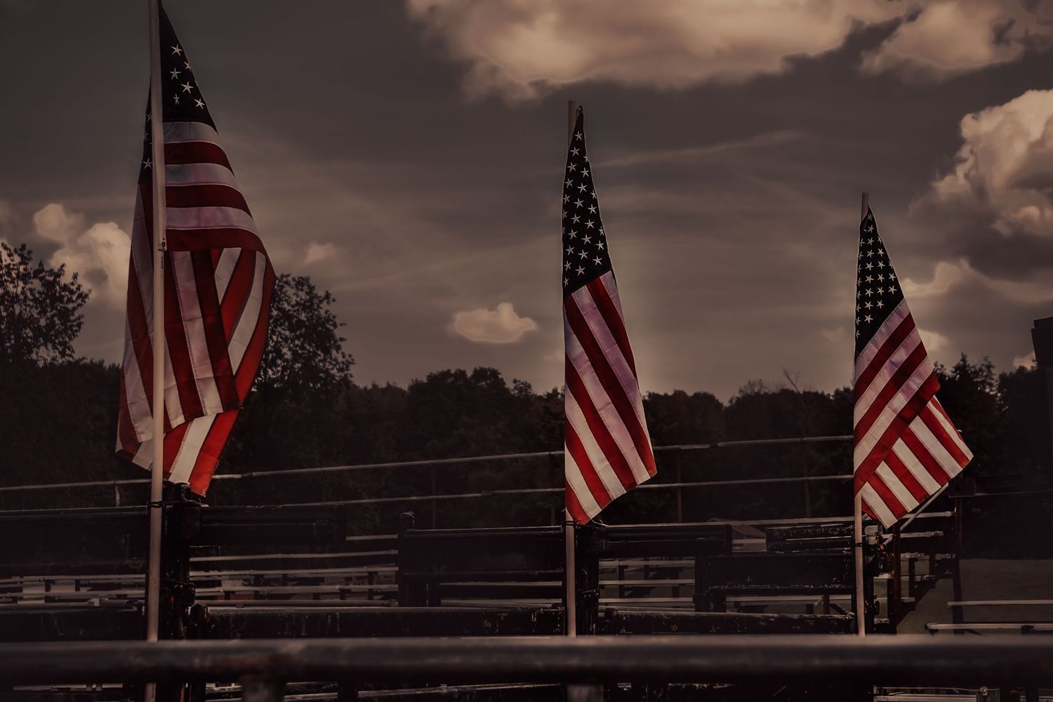 Three American flags displayed on poles against a dramatic sunset sky.