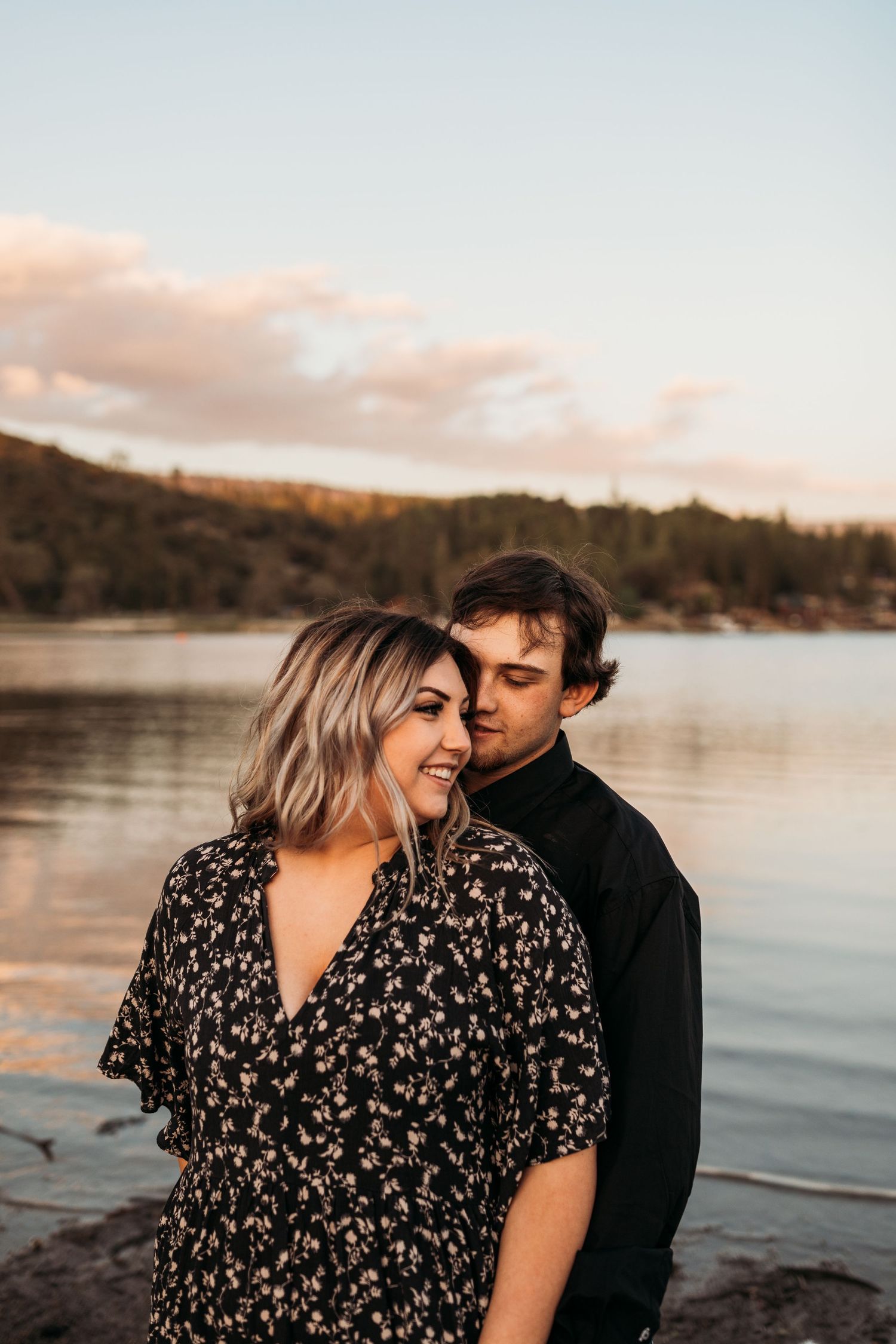 Romantic couple sharing intimate moment by lakeside during sunset.