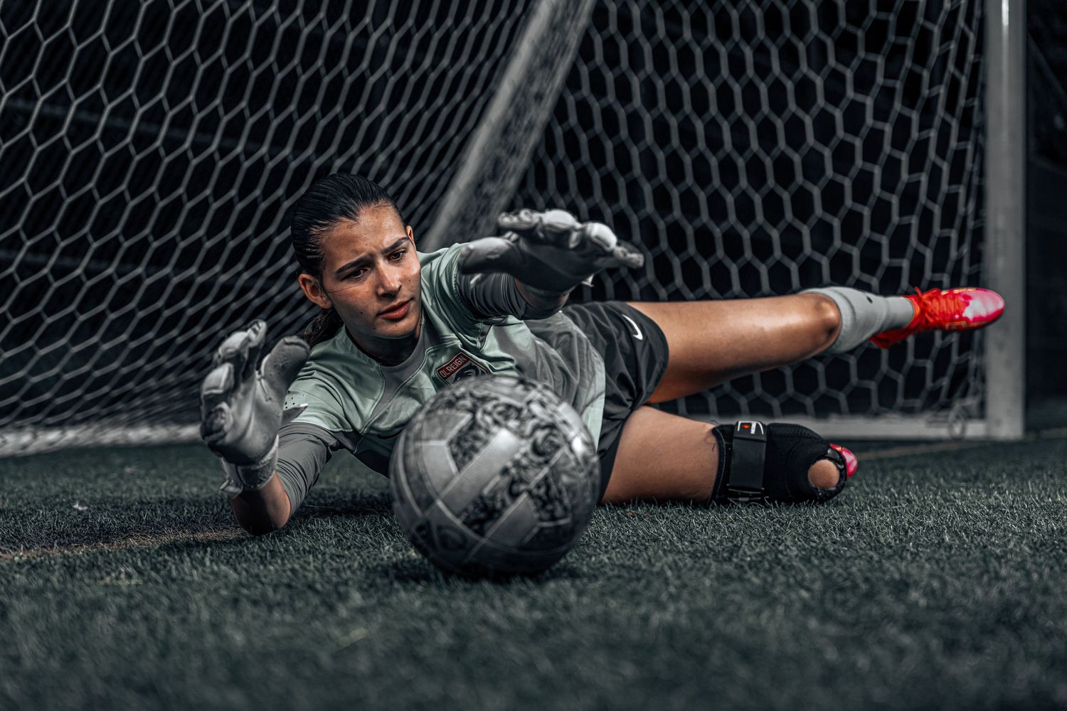 A female goalkeeper from Reign Academy soccer club making a diving save for the ball.