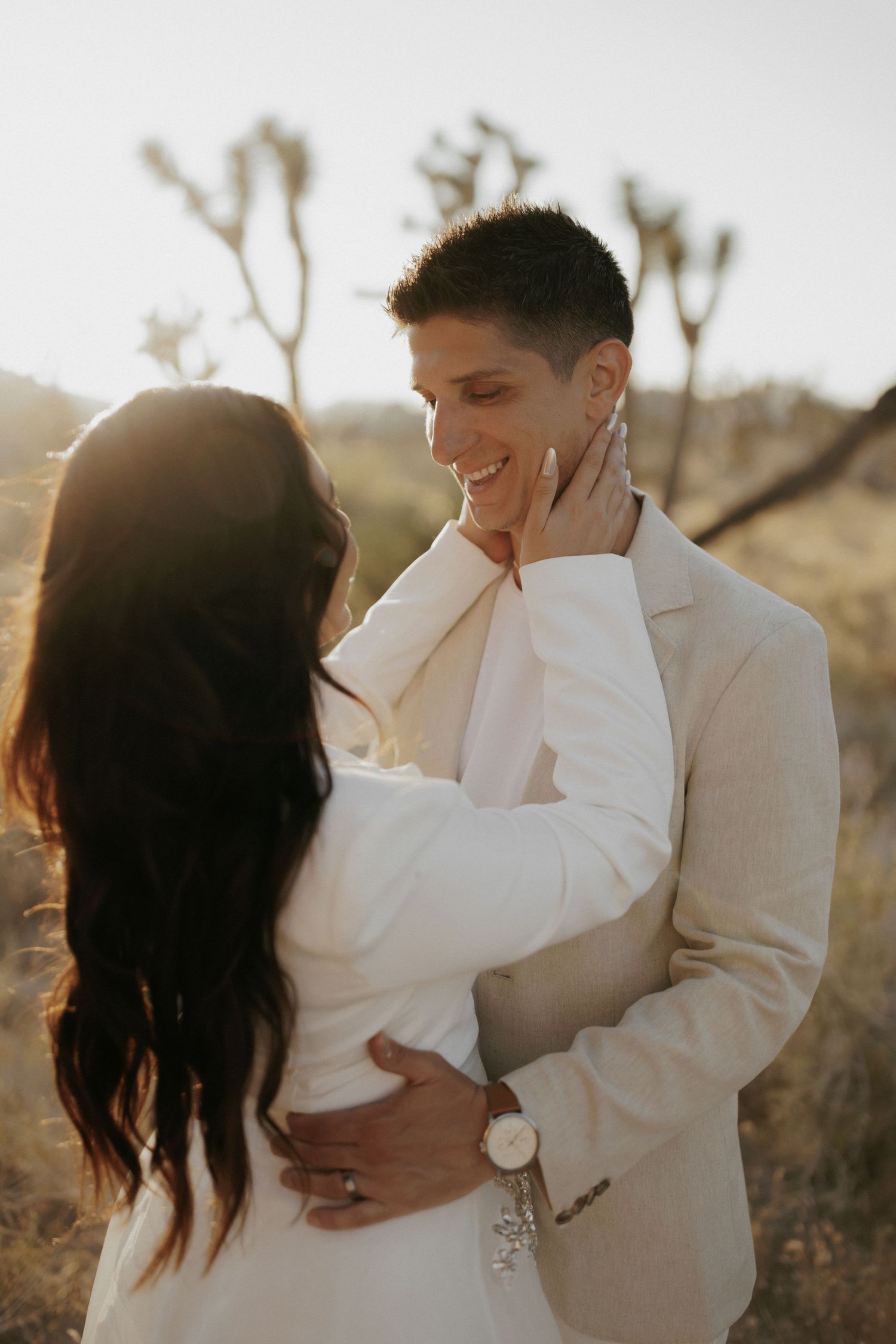 Tender moment between couple in matching white outfits in desert setting.