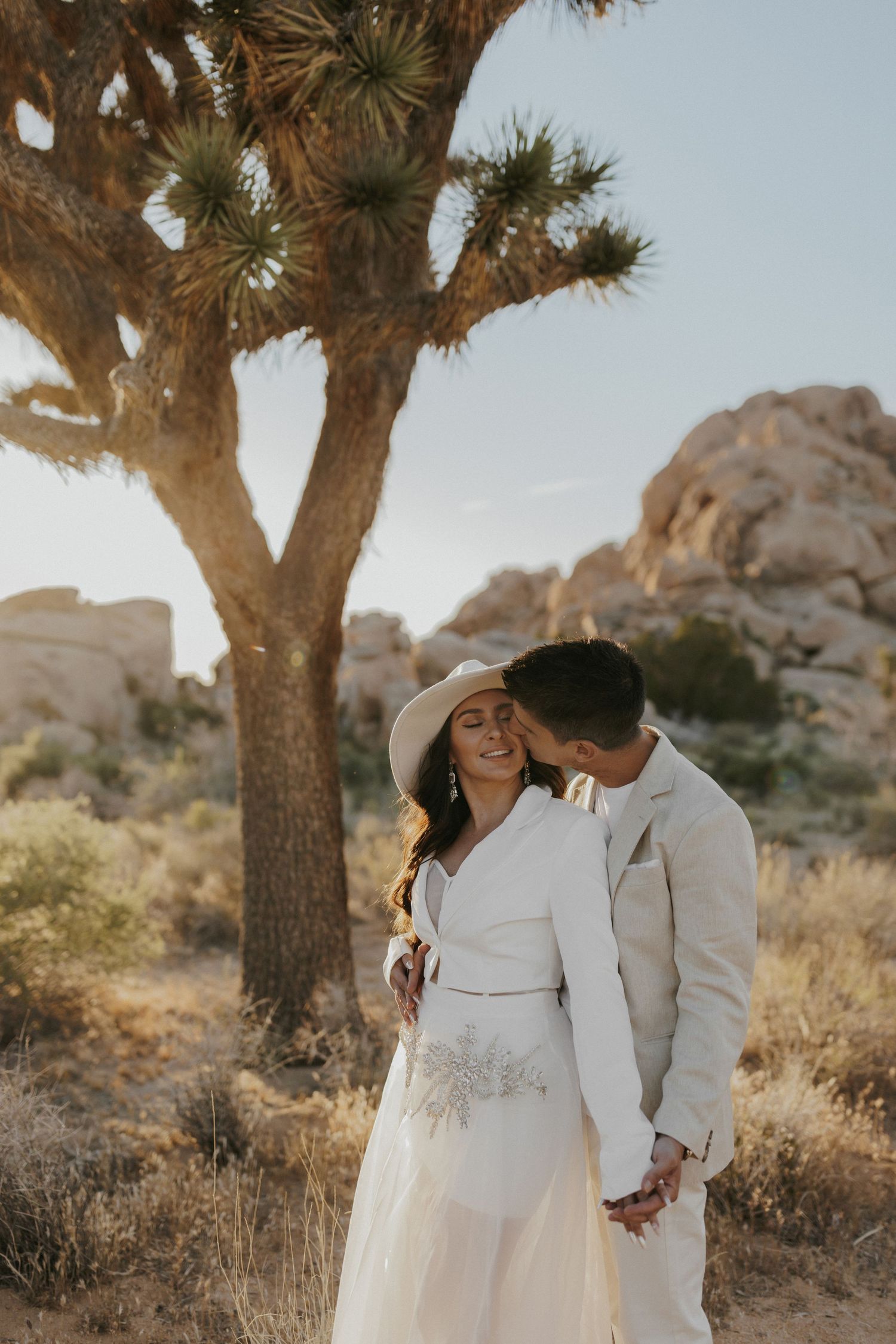 Couple in white outfits sharing intimate moment under Joshua tree.