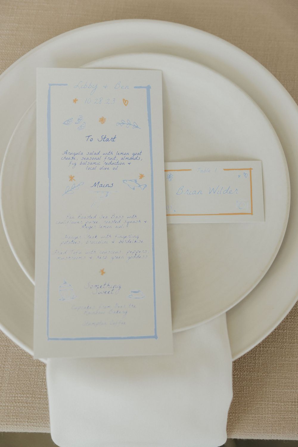 Elegant wedding menu card with blue accents on white plate against beige tablecloth.