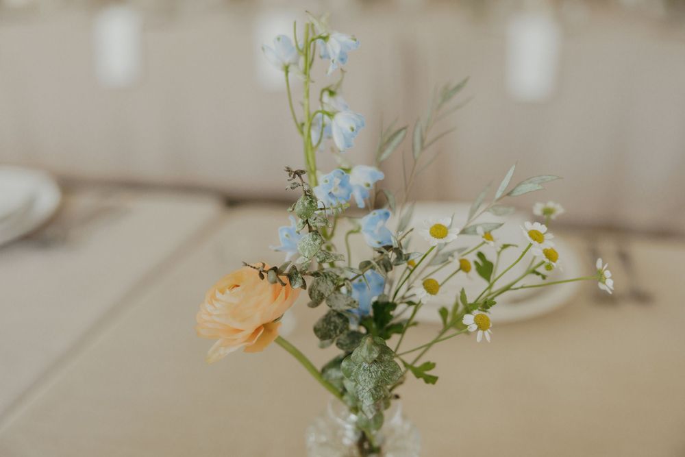 Delicate floral centerpiece with white daisies and peach flowers in glass vessel.
