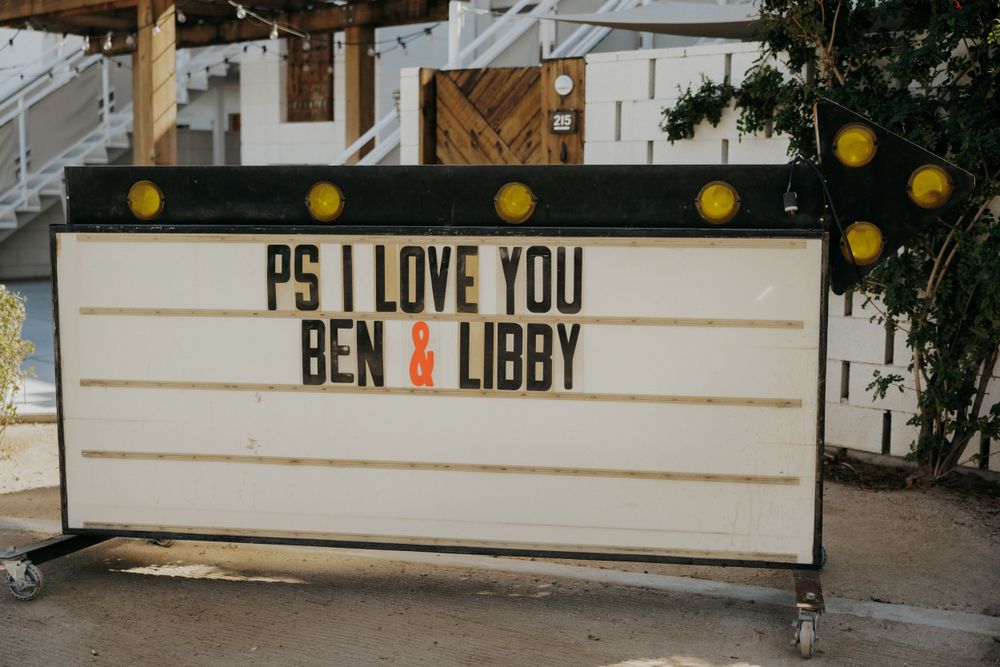 Illuminated message board displaying 'PS I LOVE YOU BEN & LIBBY' at a wedding venue.