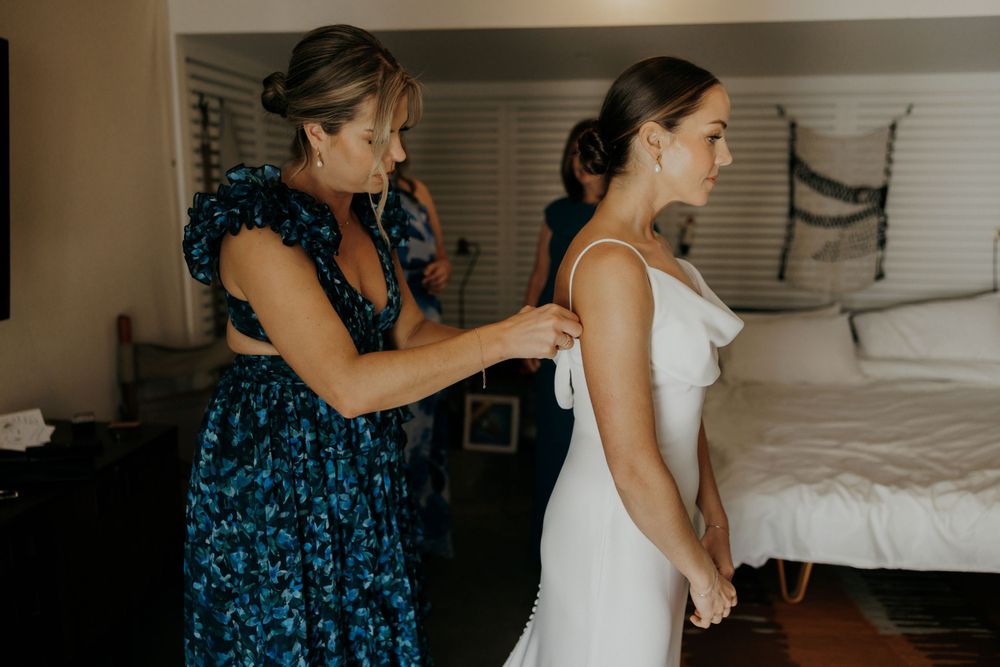 A wedding dress being fastened by someone wearing a blue patterned dress.