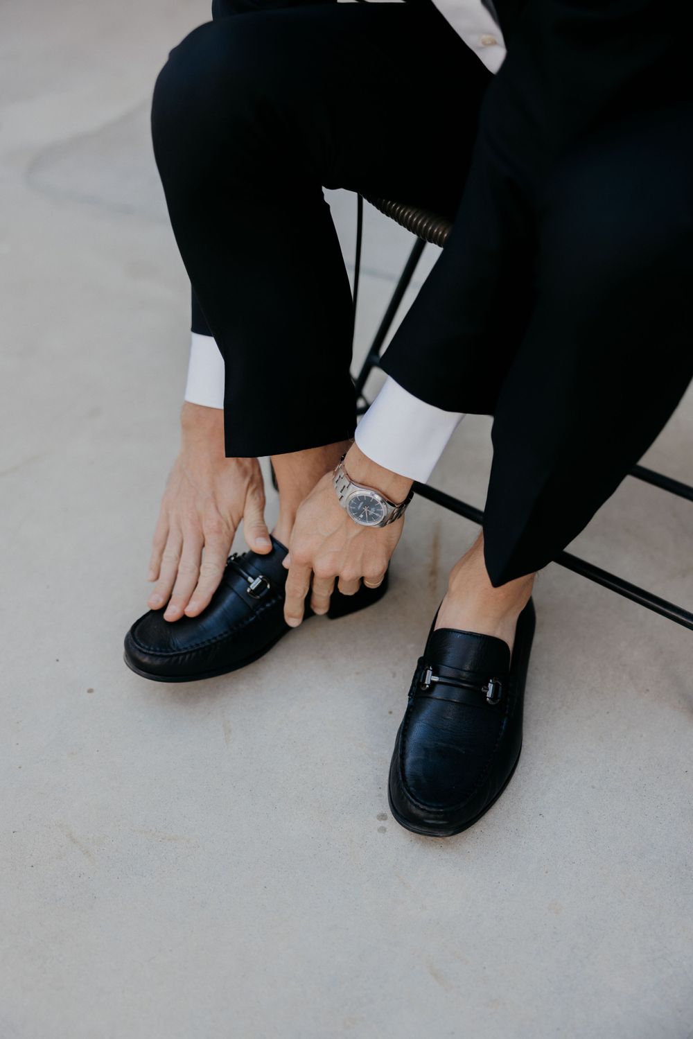 Detail shot of black formal shoes and hands adjusting the laces against a light floor.