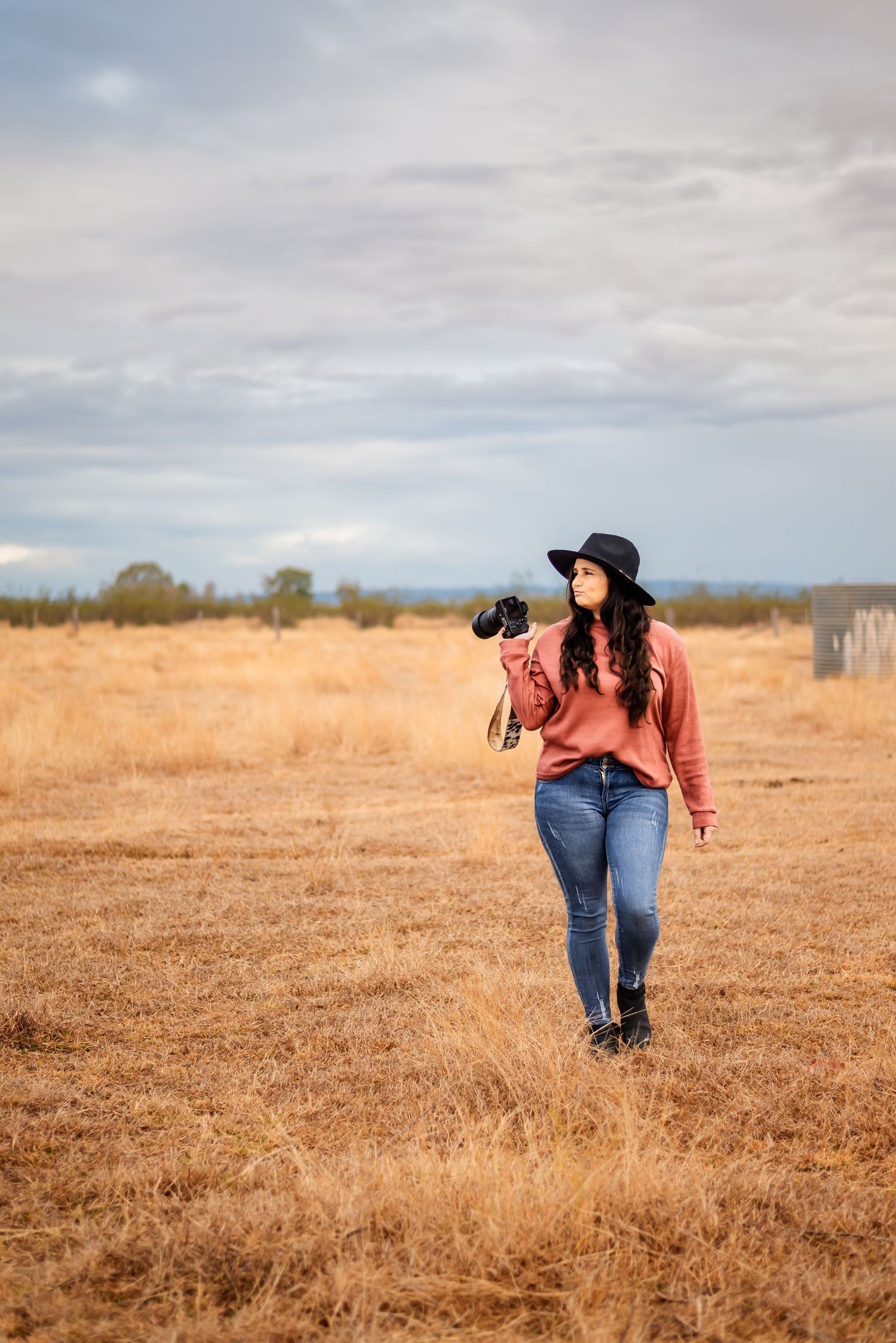 Photographer walks through golden field carrying camera equipment at dusk.