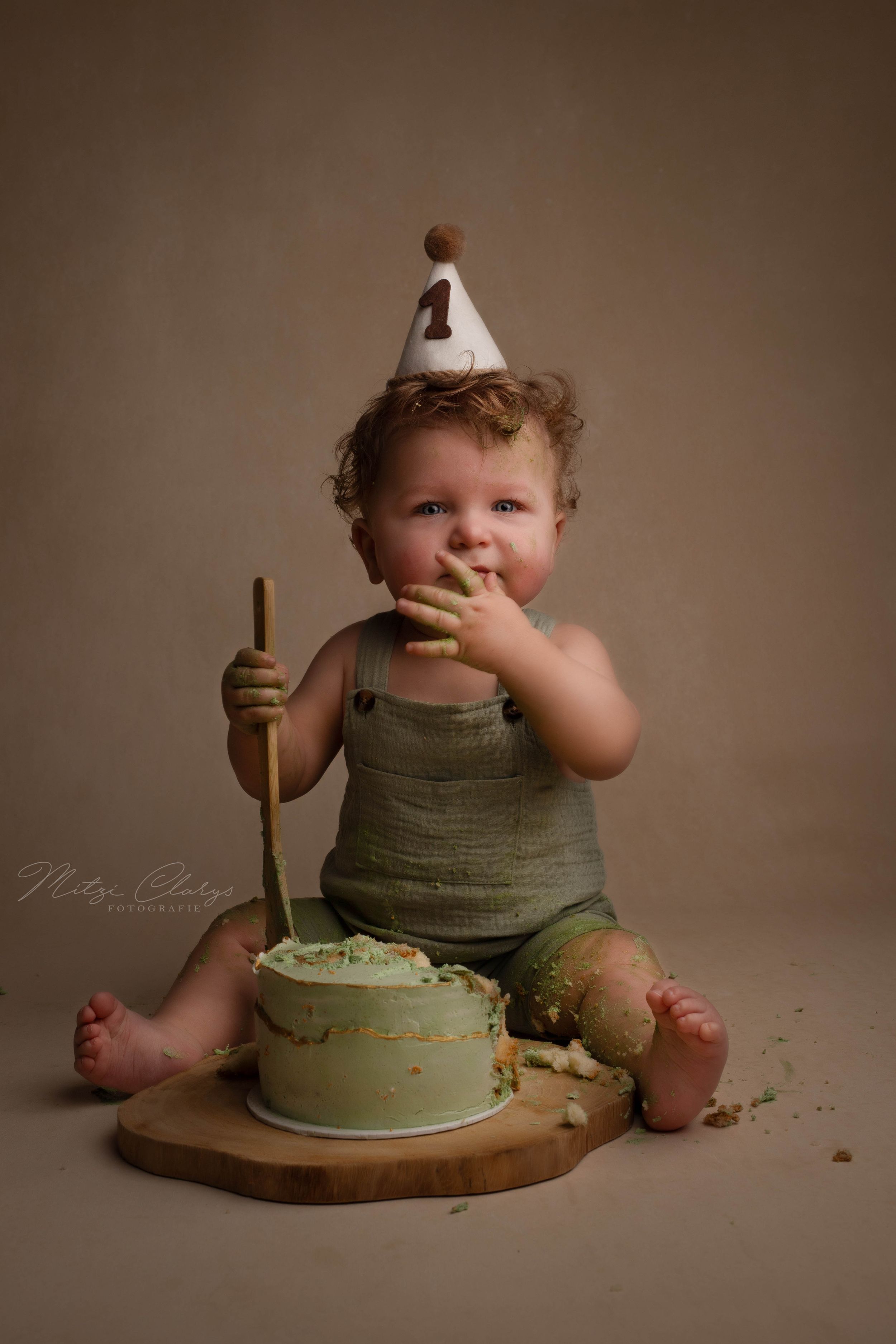 eenjarig jongetje in groen pakje proeft taart tijdens cakemash fotoshoot