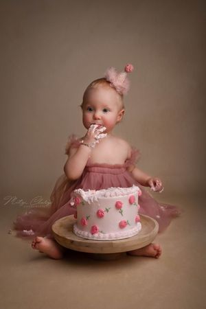 Eenjarig meisje met roze taart en feesthoedje tijdens cakesmash fotoshoot