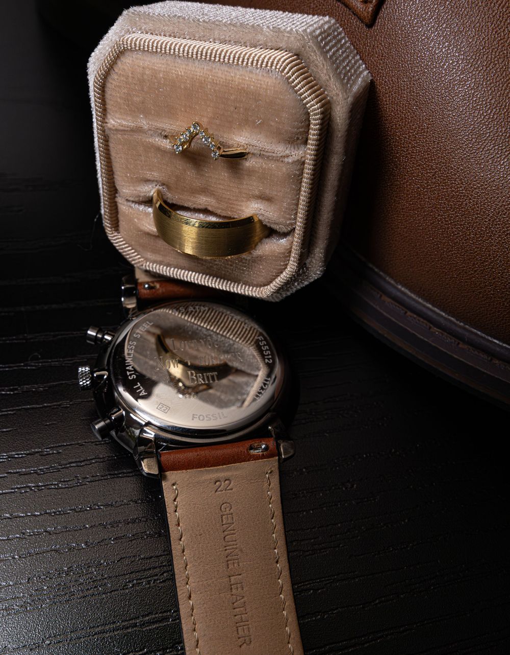 A pair of black leather shoes reveals intricate stitching details and brown leather lining on a dark wooden surface.