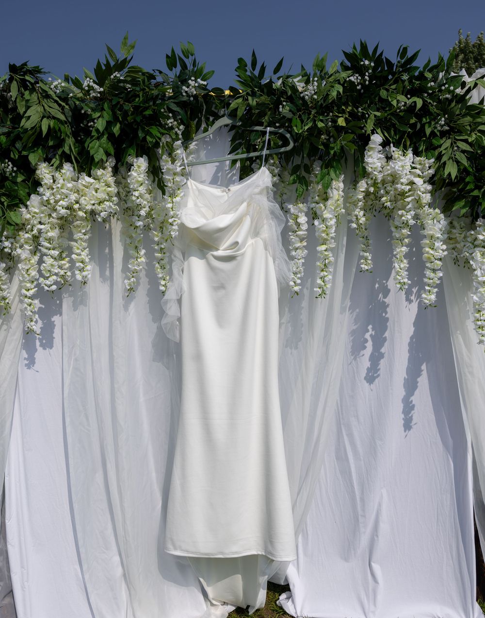 White laundry hanging to dry against a backdrop of green foliage and wisteria flowers creates a serene garden scene.