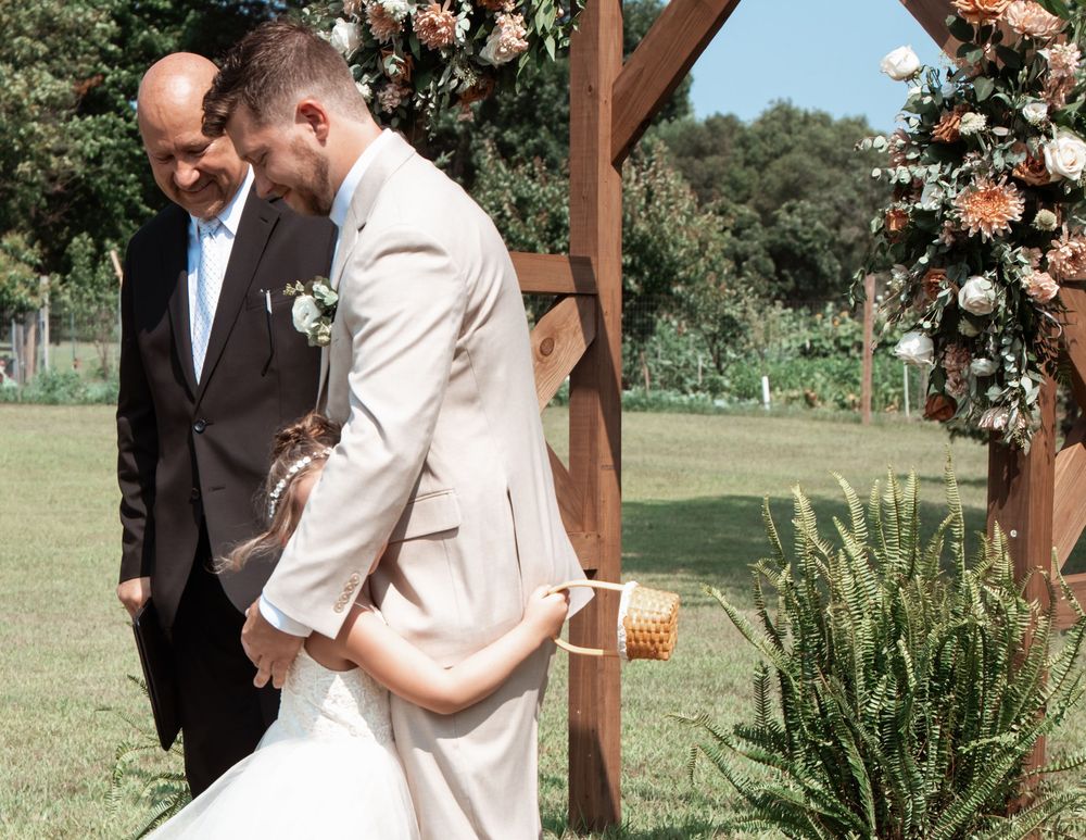Outdoor wedding ceremony under wooden arch decorated with peach roses in rustic garden setting.