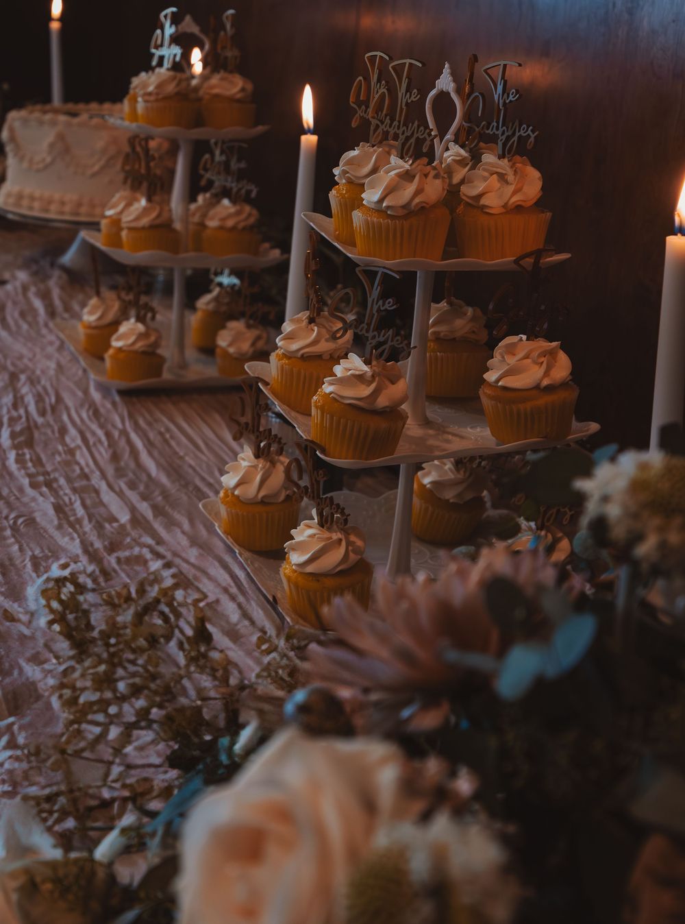 Elegant tiered cupcake display with white frosted cupcakes and soft lighting at wedding reception.