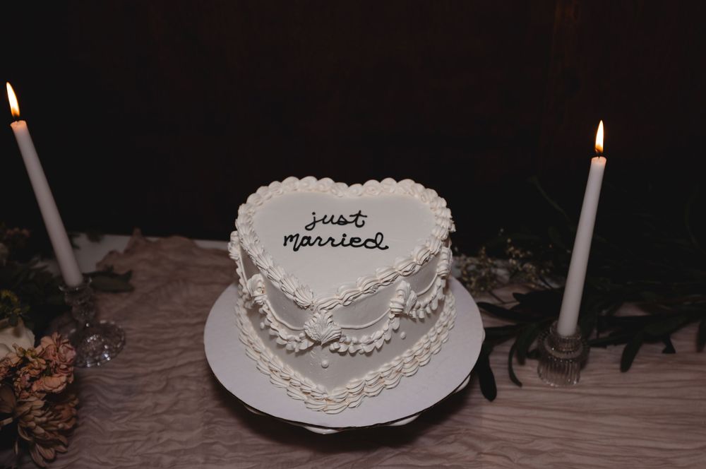 A white decorated cake with candles glows in dim lighting against a dark background.