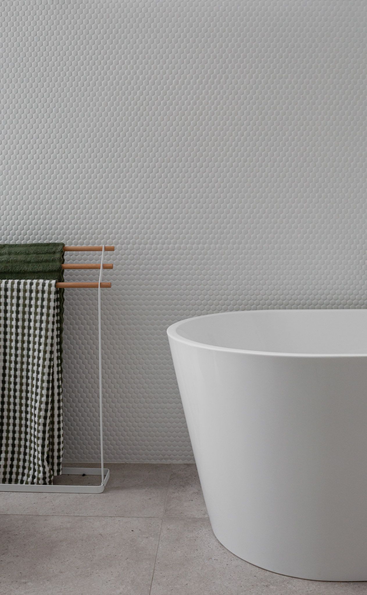 Modern bathroom featuring a freestanding white tub and textured wall with green towels.