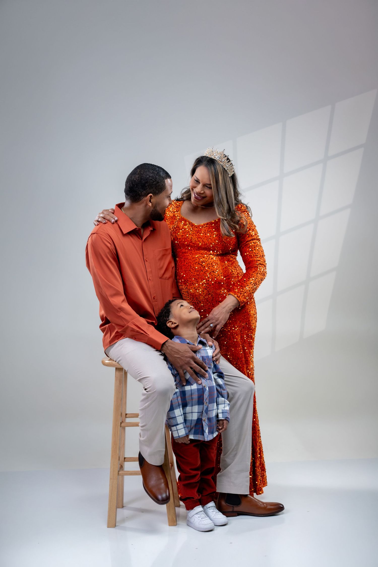 A pregnant woman in an orange dress poses with her husband and young son in a warm family maternity photo shoot.