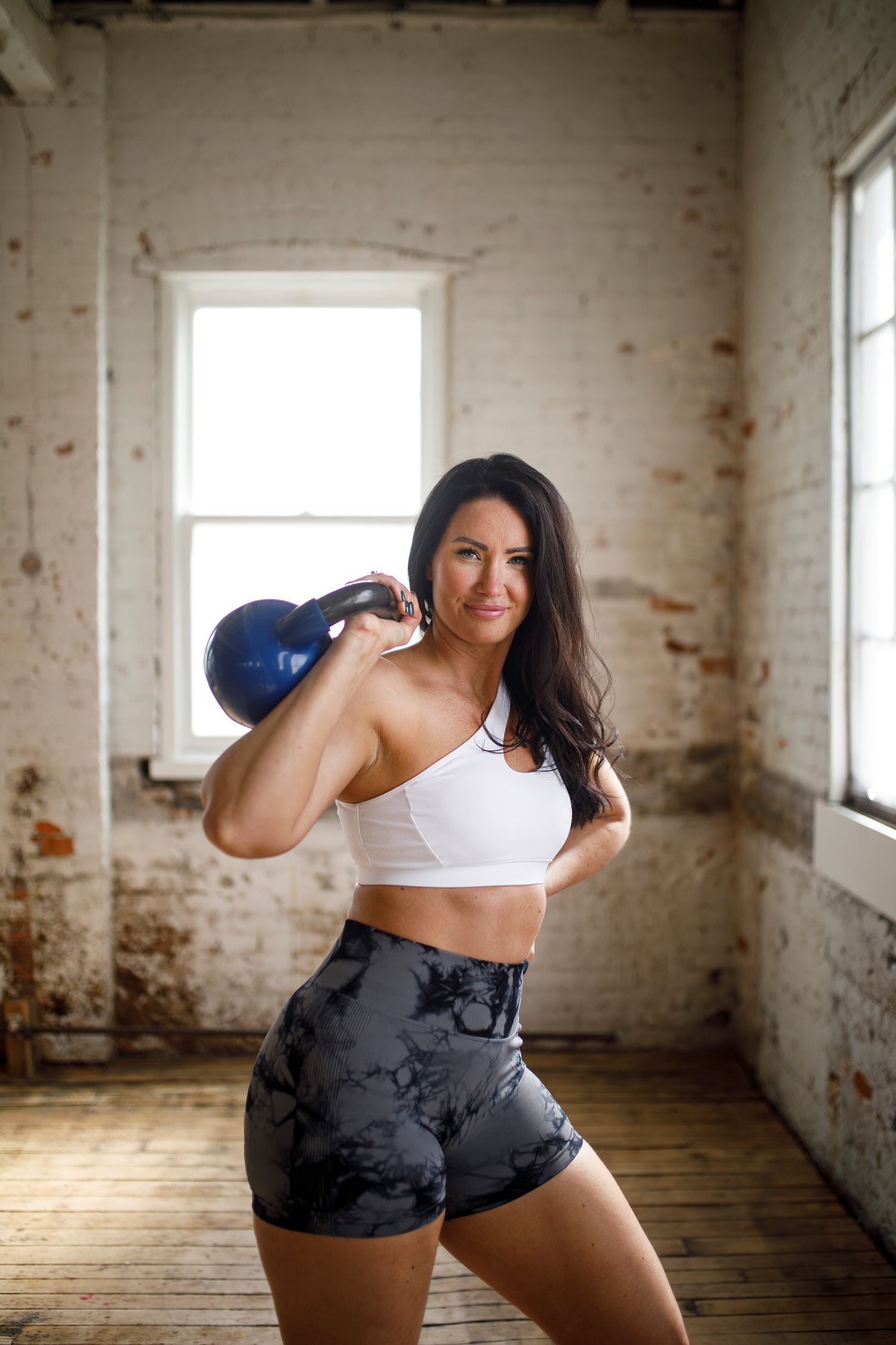 Athletic woman exercising with kettlebell in rustic warehouse studio setting.