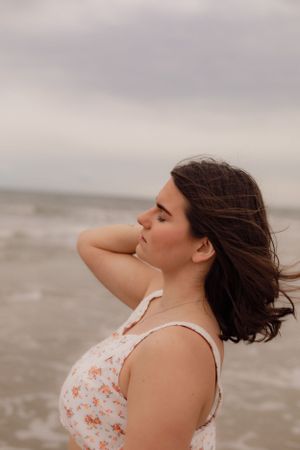 Person in a floral dress enjoying a cloudy day at the beach with hair blowing in the wind.