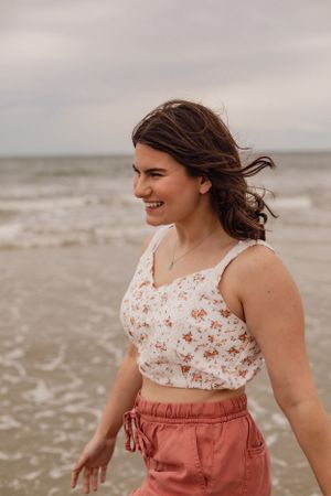 Person in floral top and coral shorts playing and laughing on a cloudy beach.