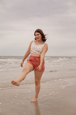 Playful beach portraits of someone splashing and dancing in coral shorts and floral top.