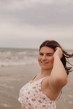 Joyful beach photoshoot featuring someone in a floral top against cloudy skies.
