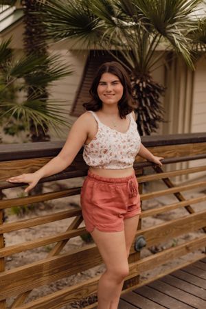 Casual summer outfit with floral crop top and coral shorts on a wooden deck with palm trees.