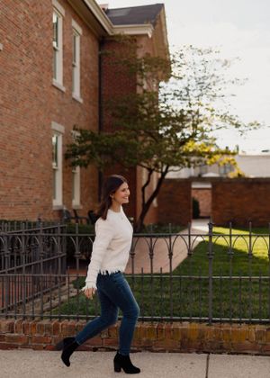 Fashion portrait showing white sweater and jeans against brick building backdrop.
