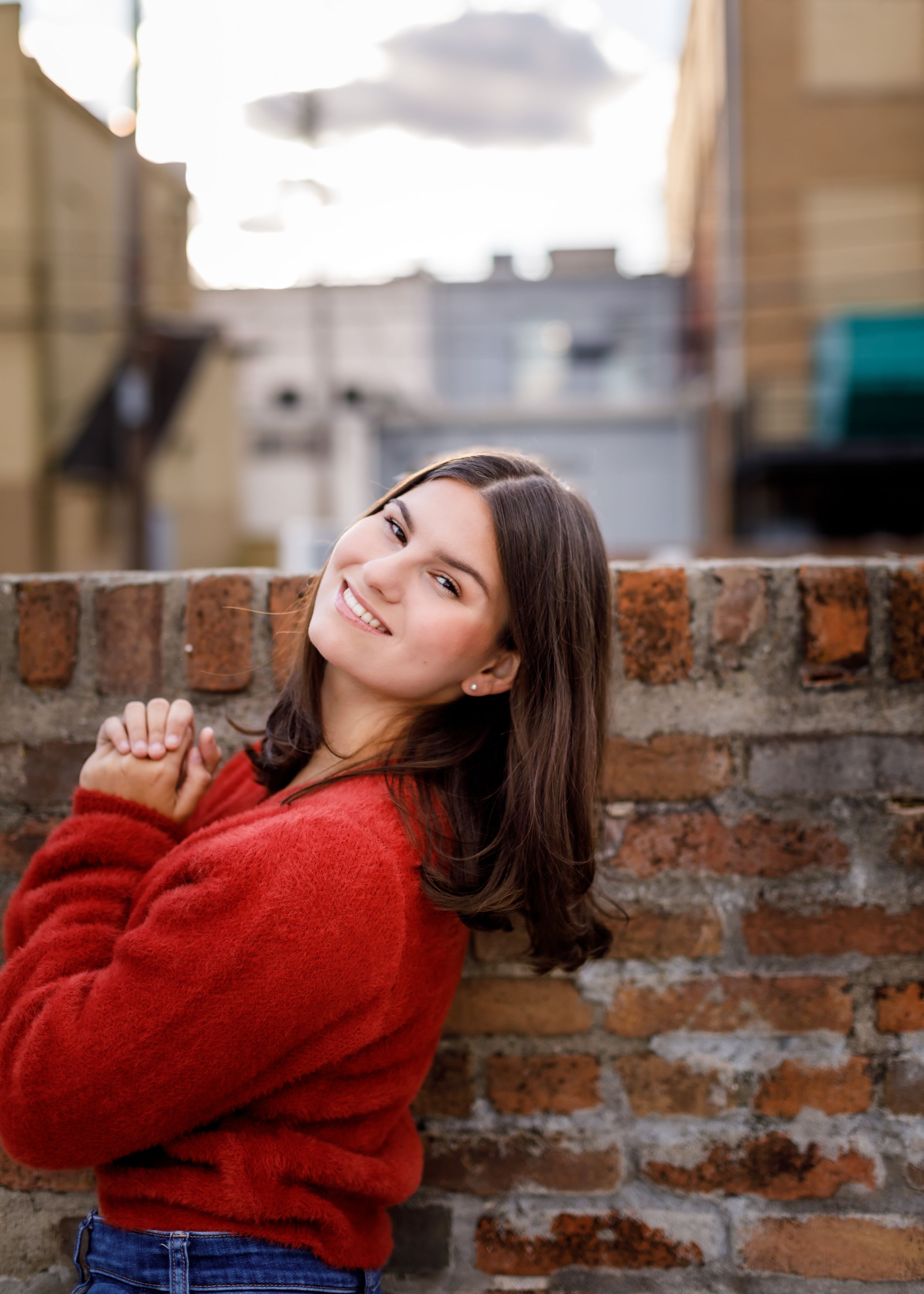 A person in a cozy red sweater poses playfully against a brick wall in a series of candid shots.